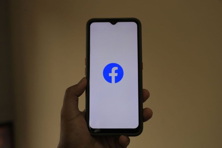 Mão segurando um smartphone com o logotipo do Facebook na tela