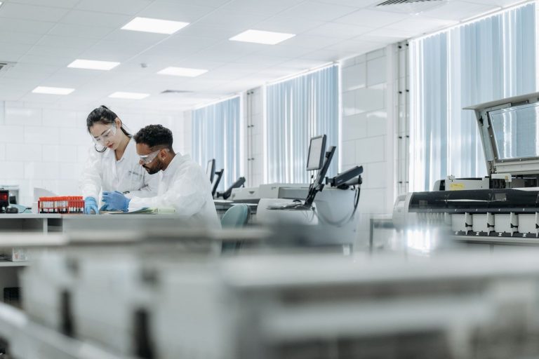 Dois cientistas usam equipamentos de proteção e trabalham juntos em um laboratório de alta tecnologia.